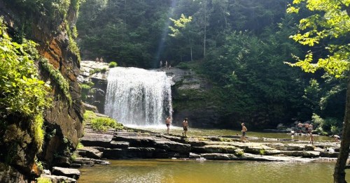A crowd of people on the rocky edges of the natural waterfall pool at Compression Falls in Tennessee.