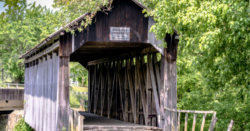 Closeup of the entrance of a wooden covered bridge surrounded by trees on a sunny day in kentucky