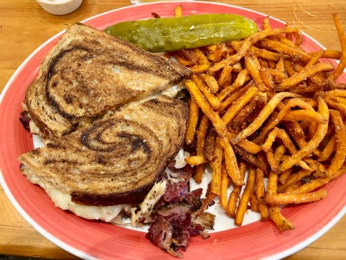 A plate featuring a grilled sandwich, a pickle, and a side of crispy sweet potato fries.