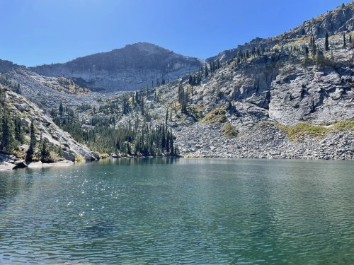 A serene lake surrounded by rocky cliffs and lush greenery under a clear blue sky.