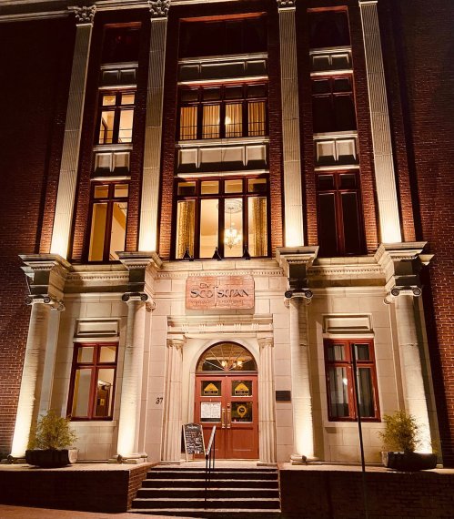 Historic building facade with illuminated windows, featuring a central entrance and decorative architectural details.