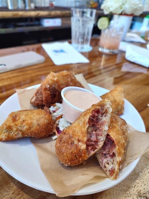 A plate of crispy fried snacks filled with meat and cabbage, served with a dipping sauce on the side.