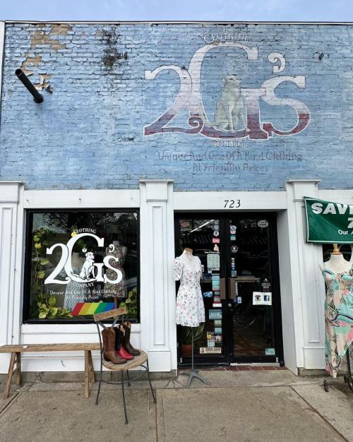 Storefront of "2 G's" featuring a dress on display, boots, and a mural on the brick wall above.