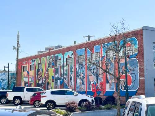 Colorful mural on a brick wall featuring the word "FIVE POINTS" with various artistic elements and parked cars in front.