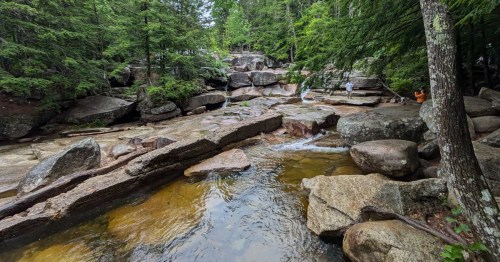 A serene rocky landscape with a flowing stream surrounded by lush green trees.