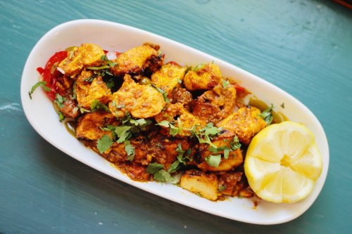 A dish of spiced chicken garnished with herbs, served with lemon wedges on a white plate.