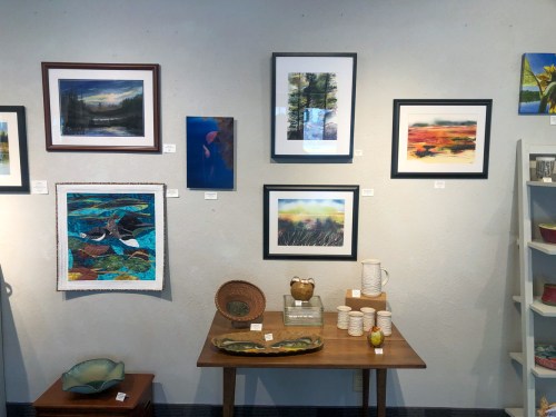 A gallery wall featuring various framed artworks, a wooden table with decorative items, and pottery on display.
