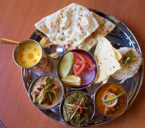 A silver platter with various Indian dishes, including naan, rice, curries, and fresh vegetables.