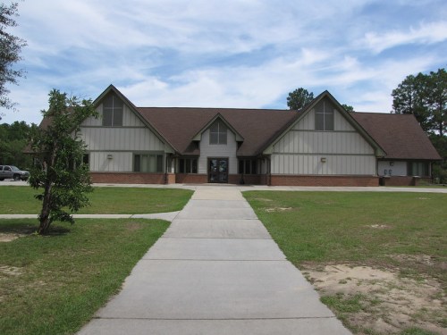 A large, modern building with a sloped roof, surrounded by grass and a walkway leading to the entrance.