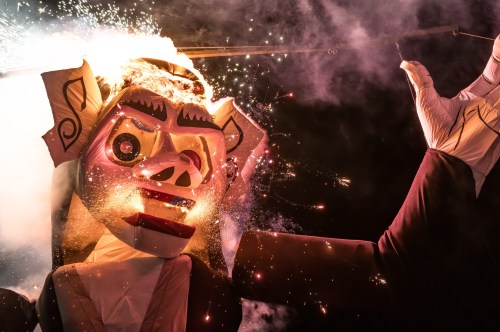A large, colorful puppet with a pig-like face, surrounded by sparks and smoke, creating a festive atmosphere.