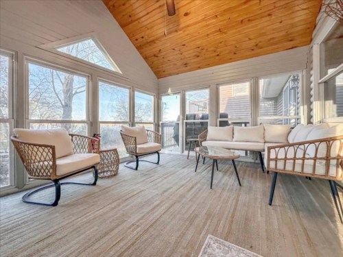 Bright sunroom with large windows, cozy seating, and wooden ceiling, creating a warm and inviting atmosphere.