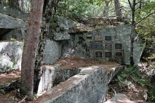 A rocky area in a forest with several plaques mounted on the stone, surrounded by trees and greenery.