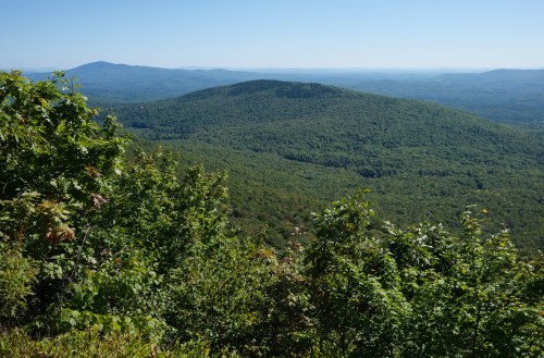 A panoramic view of lush green mountains under a clear blue sky, with rolling hills in the distance.