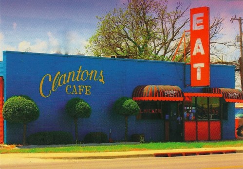 A colorful cafe with a blue exterior, red signage reading "EAT," and neatly trimmed bushes in front.