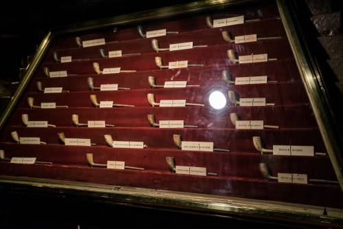 A display case featuring various pipes, each labeled with names, set against a red velvet background.