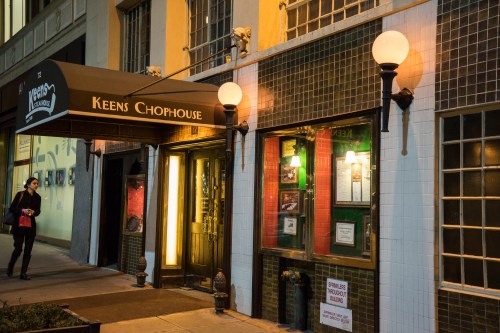 Exterior of Keens Chophouse at night, featuring a canopy, warm lighting, and a person walking by.