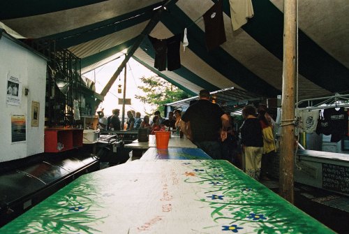 A bustling tent with people socializing, colorful decorations, and a painted table in the foreground.