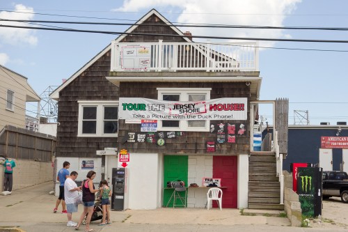 A beach house with a sign promoting tours, featuring colorful doors and people walking by.