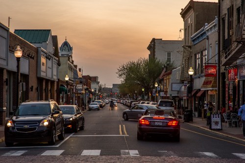A bustling street at sunset, lined with shops and cars, creating a lively urban atmosphere.