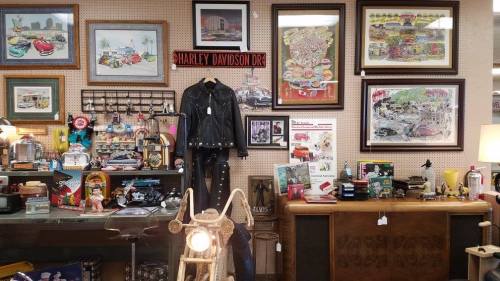 A vintage shop display featuring memorabilia, artwork, and collectibles, including a leather jacket and retro decor.