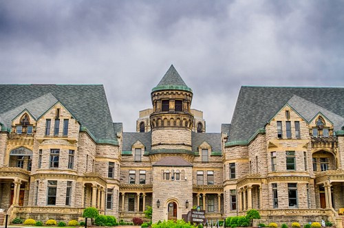 Historic stone building with a turret, intricate architecture, and a cloudy sky in the background.
