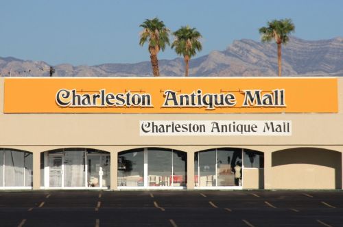 Sign for Charleston Antique Mall with palm trees and mountains in the background. Clear blue sky above.