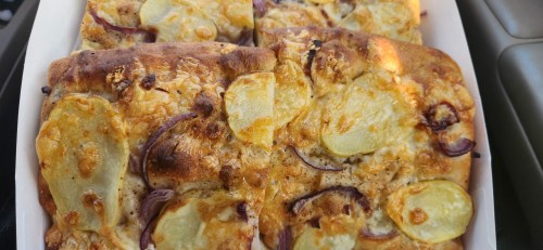 A close-up of a rectangular pizza topped with cheese, sliced potatoes, and red onions, in a white box.
