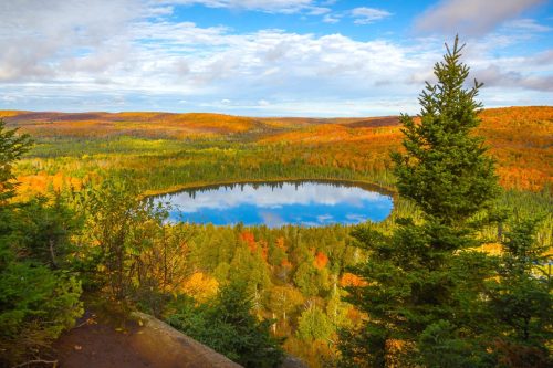 A serene lake surrounded by vibrant autumn foliage and rolling hills under a partly cloudy sky.
