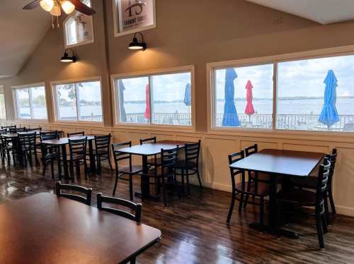 Interior of a restaurant with empty tables and a view of a lake through large windows, featuring colorful umbrellas outside.
