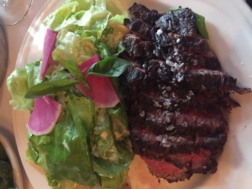 A plate featuring grilled steak with a sprinkle of salt, accompanied by a fresh salad with lettuce and radish slices.