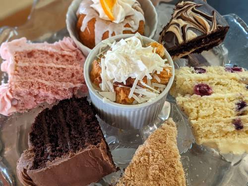 A variety of cakes and desserts arranged on a glass platter, including chocolate, strawberry, and coconut flavors.
