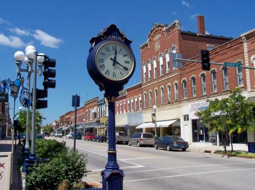 A historic downtown street with a large clock, shops, and clear blue skies in Anamosa, Iowa.