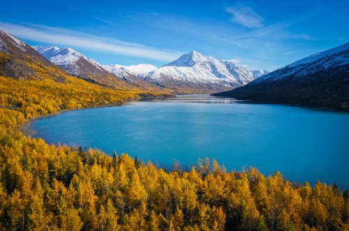 A serene lake surrounded by vibrant autumn trees and snow-capped mountains under a clear blue sky.