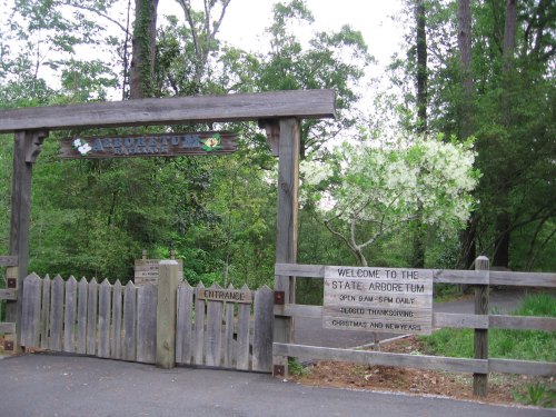 Entrance to a state arboretum, featuring a wooden gate and signs about visiting hours and special events.