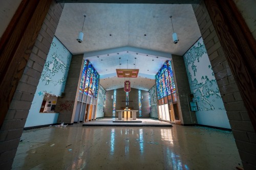Abandoned interior of a church with stained glass windows, peeling walls, and a central altar.