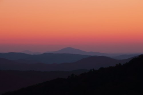 A serene sunset over layered mountains, with soft pink and orange hues blending into the sky.