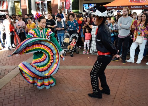A colorful traditional dance performance in a lively outdoor setting, with a crowd watching and enjoying the show.