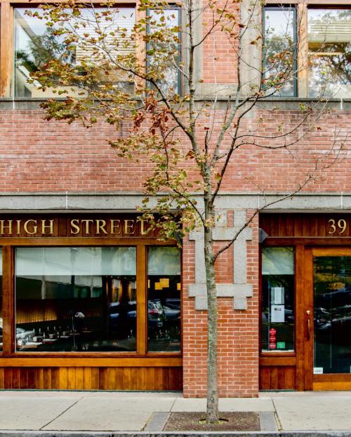 A brick building with large windows, featuring a small tree in front and a sign that reads "HIGH STREET."
