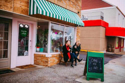 Two women sit outside a café with a green sign, enjoying drinks and chatting under a striped awning.