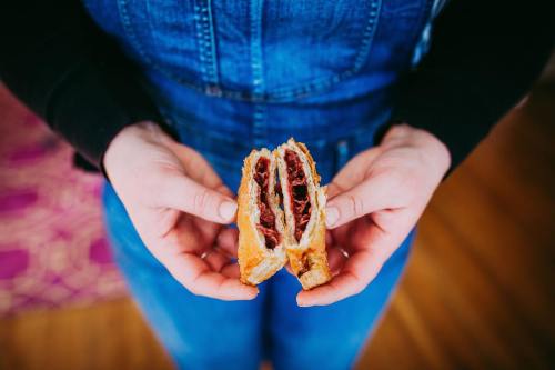 A person in denim overalls holds a sliced pastry revealing a rich, dark filling.