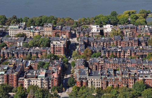 Aerial view of a historic urban neighborhood with brick buildings and tree-lined streets near a body of water.