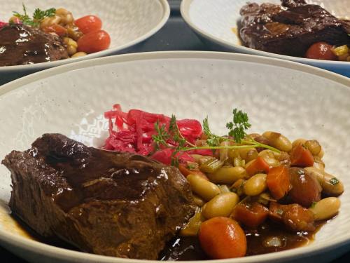 A plated dish featuring braised beef, colorful vegetables, pickled onions, and garnished with herbs in a textured bowl.