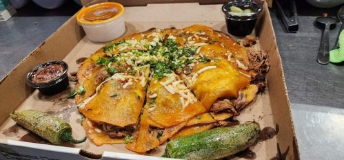 A box of cheesy enchiladas topped with beef, cilantro, and cheese, served with jalapeños and sauces on the side.