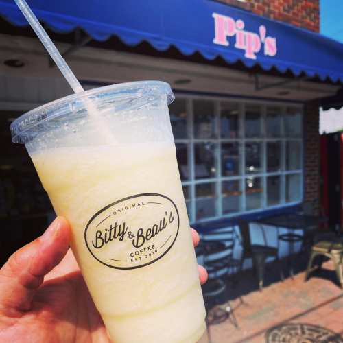 A hand holding a frozen drink from Bitty & Beau's Coffee in front of a café with a blue awning.