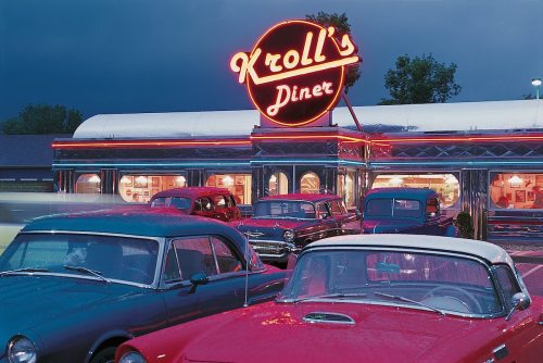 A vintage diner with a neon sign, surrounded by classic cars under a moody sky.