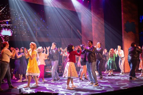A lively stage performance with dancers in colorful costumes, celebrating under vibrant lights.