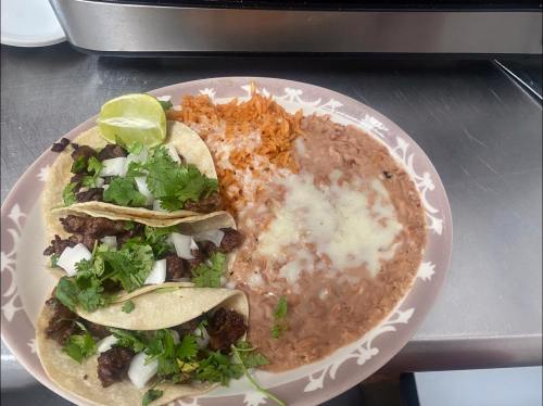 A plate of tacos with beef, onions, and cilantro, served with rice and refried beans topped with cheese and a lime wedge.