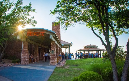 A rustic building with a sign reading "Red Rock," surrounded by trees and a gathering of people outside.