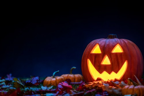 A carved pumpkin with a smiling face, glowing from within, surrounded by smaller pumpkins and colorful autumn leaves.
