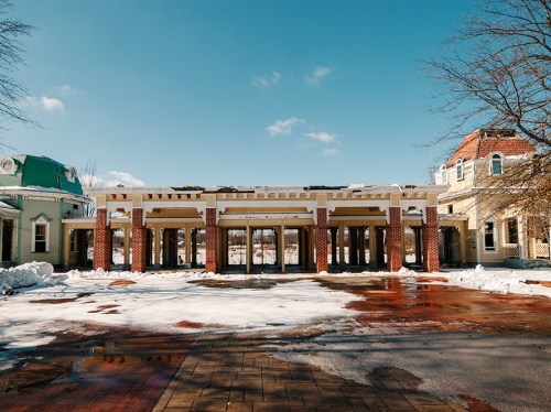 A snow-covered plaza with brick columns and a clear blue sky, surrounded by buildings.